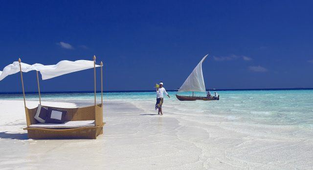 Person geht mit Getränken einen weißen Sandstrand auf den Malediven entlang